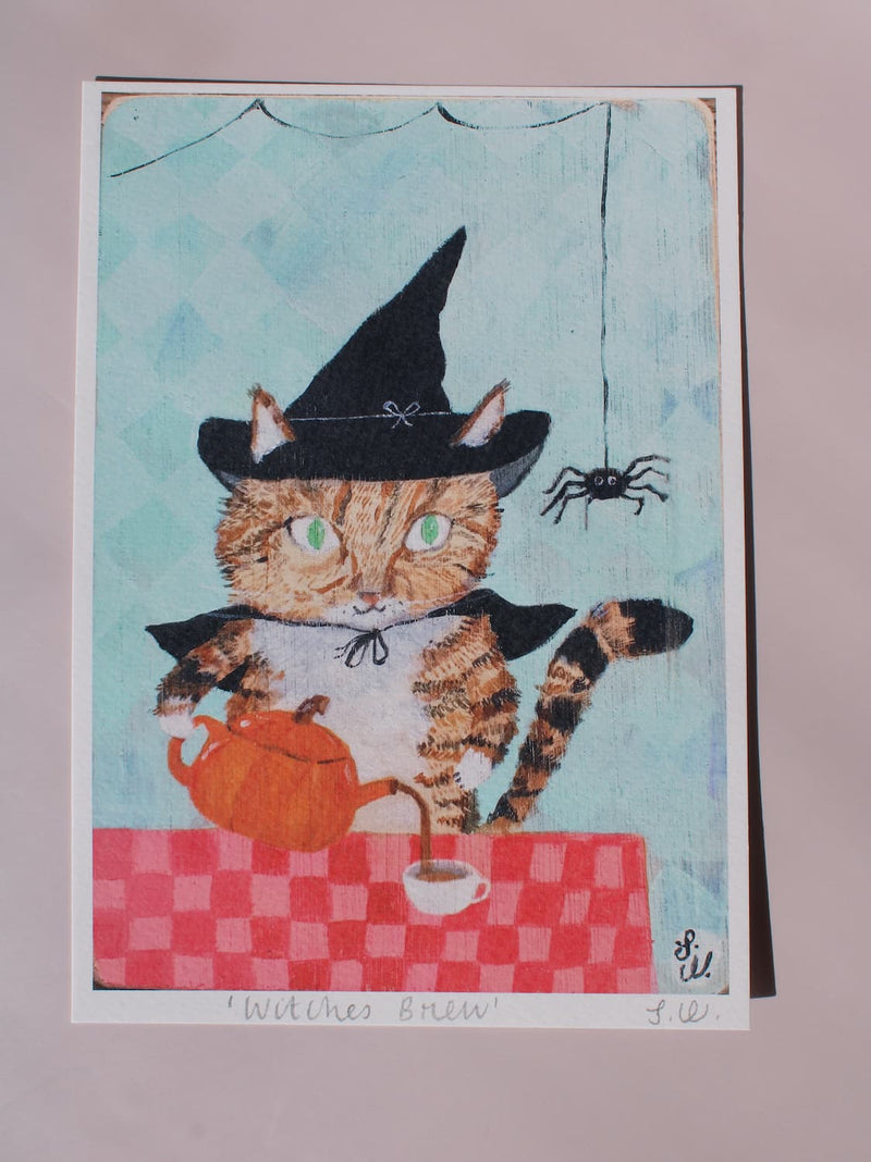 Witches Brew Cat Art Print A whimsical art print titled 'Withes Brew' featuring a tabby cat dressed as a witch holding an orange teapot behind a red checkered table. The print is mounted on a textured off-white wall.