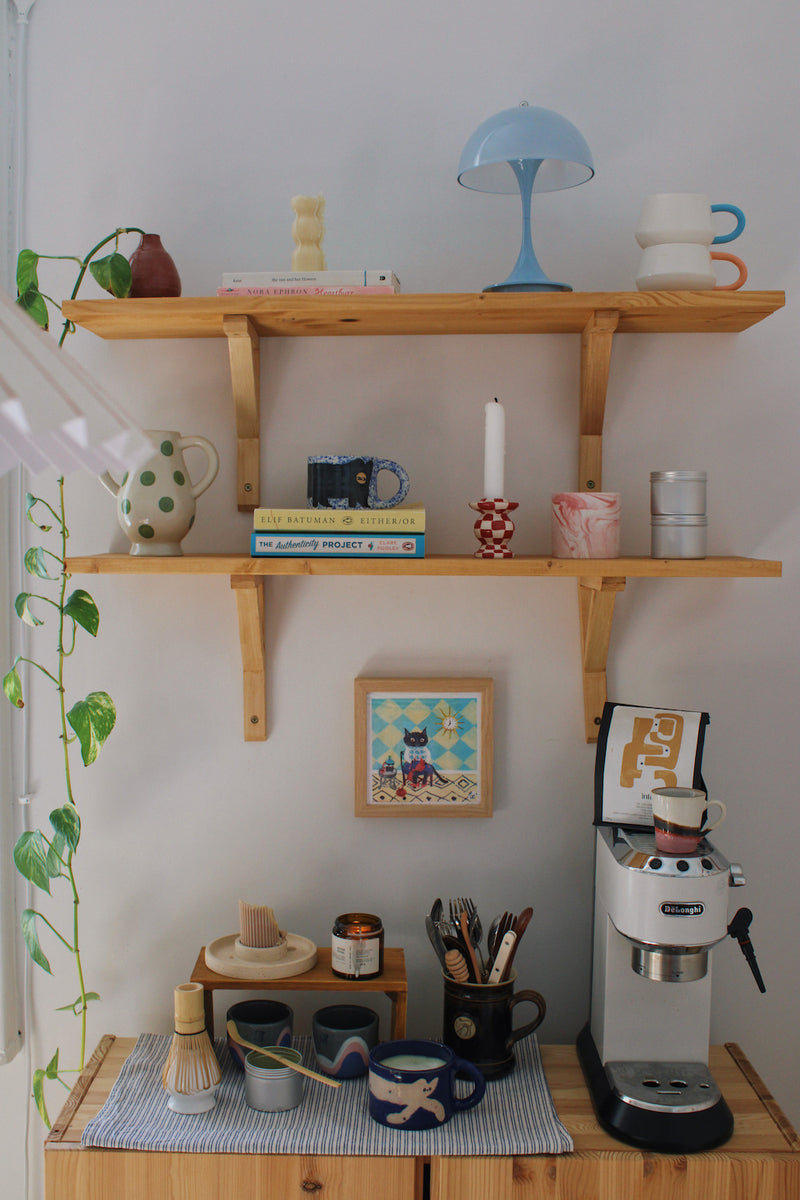 Knitting Cat Art Print – illustrated cat art print styled on a wall above a colourful coffee station with ceramic mugs, books and home decor
