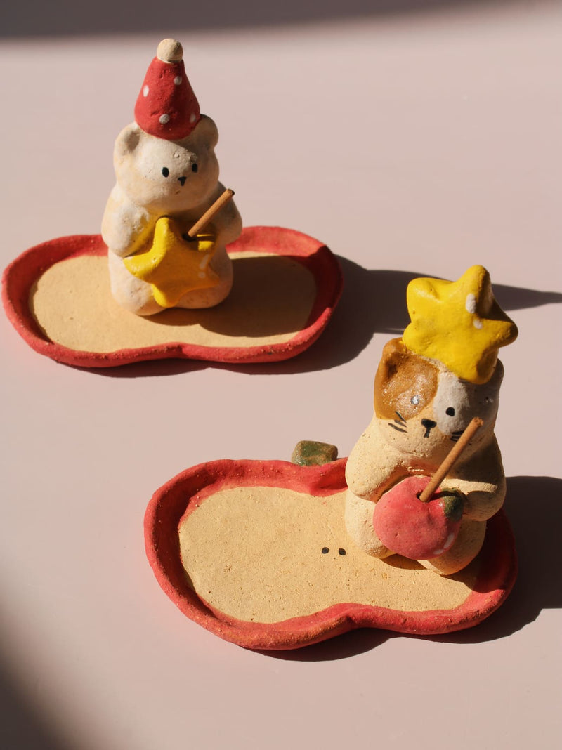 Teddy Ceramic Incense Holder and Mochi Ceramic Incense Holder, two handmade animal figurines with star and apple accents on matching apple-shaped incense trays, on a soft pink background.