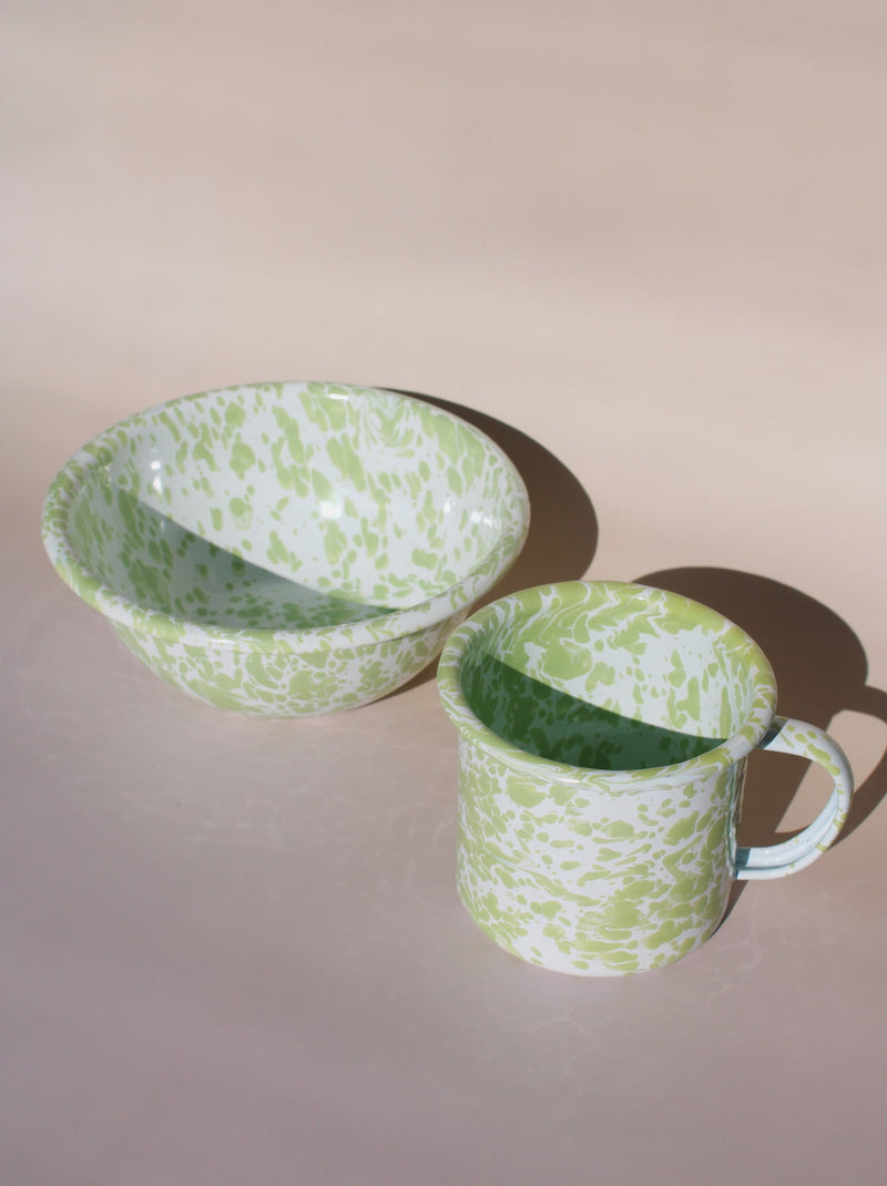 Green and white patterned clover enamel cup and bowl on a beige background