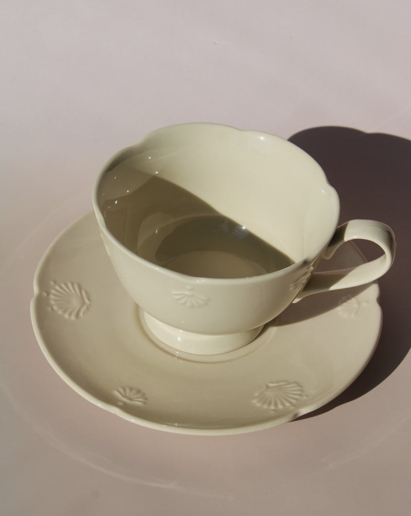Handmade Sorelle ceramic cup and saucer set in soft cream glaze with delicate embossed shell details, elegant tea cup for coffee or afternoon tea.