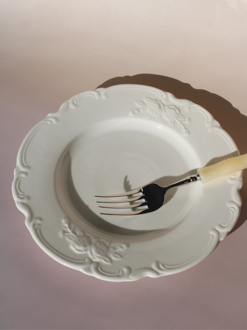 White decorative plate with a fork on a pink background