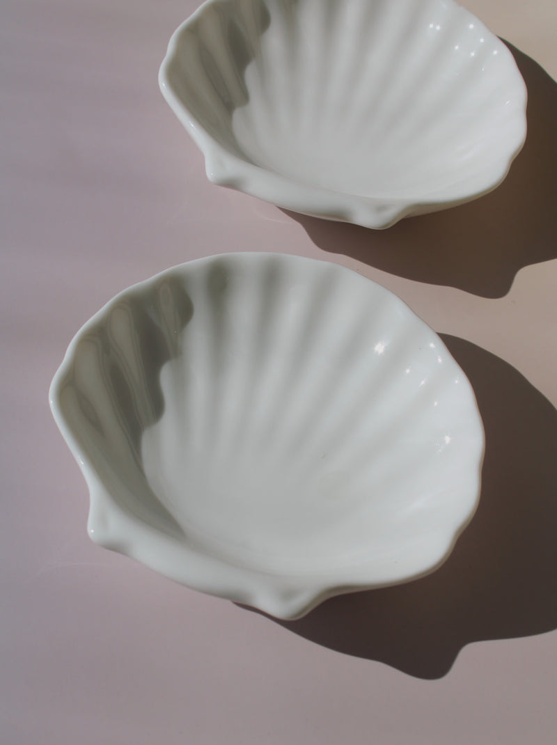Two white ceramic shell-shaped dishes on a pink background