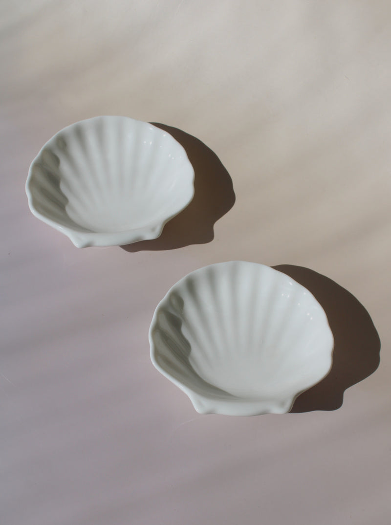 Two white ceramic shell-shaped bowls on a light pink background