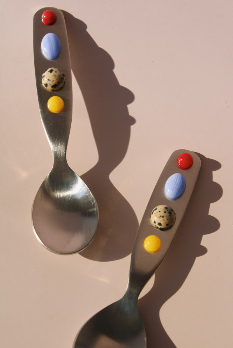 Two stainless steel dessert spoons with colorful bead handles, playful handmade style cutlery for coffee, dessert, or breakfast table.