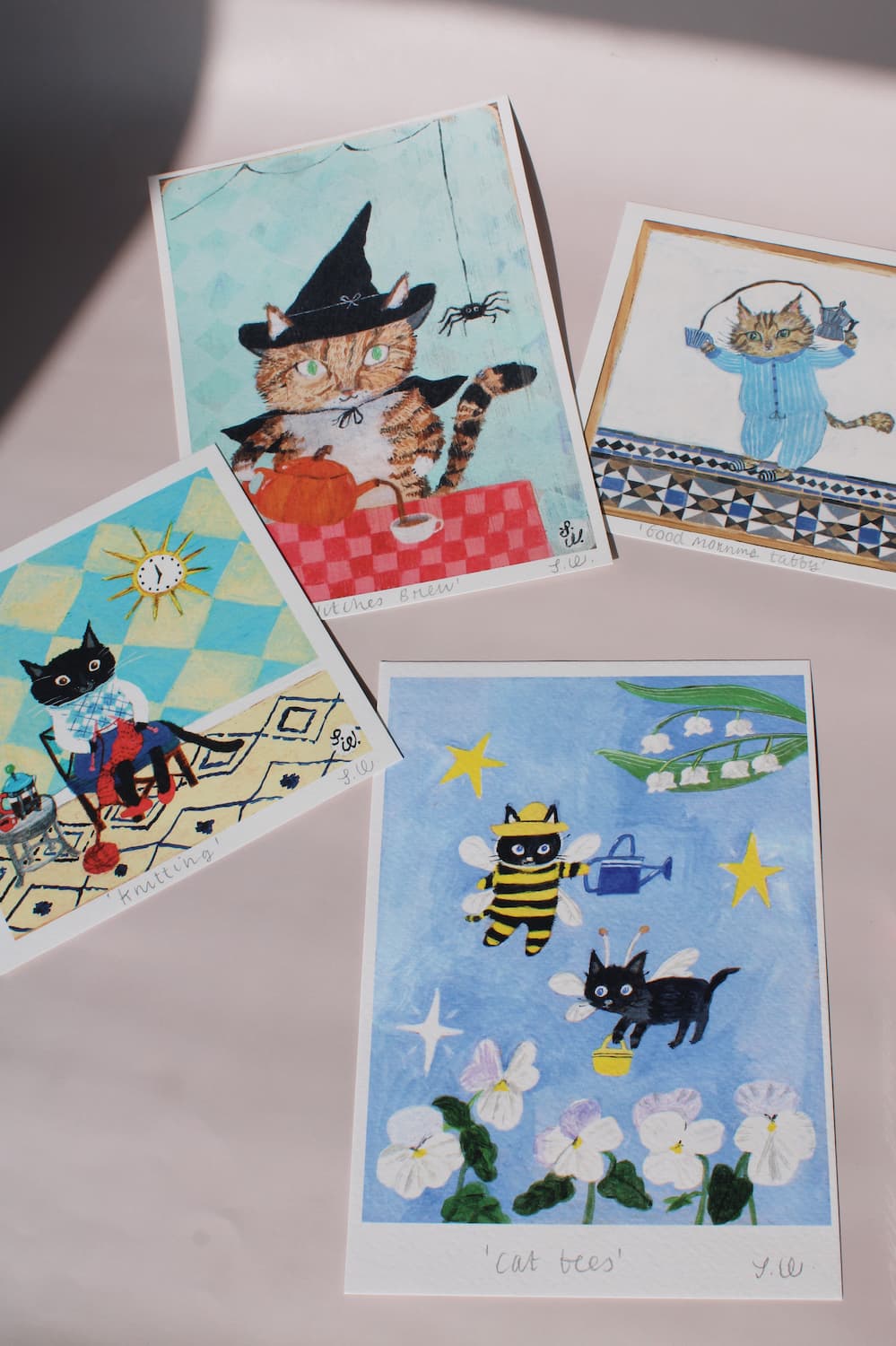 Art and paper goods collection featuring playful illustrated cat art prints, including cats dressed as witches and bees, and a cat in blue pyjamas.