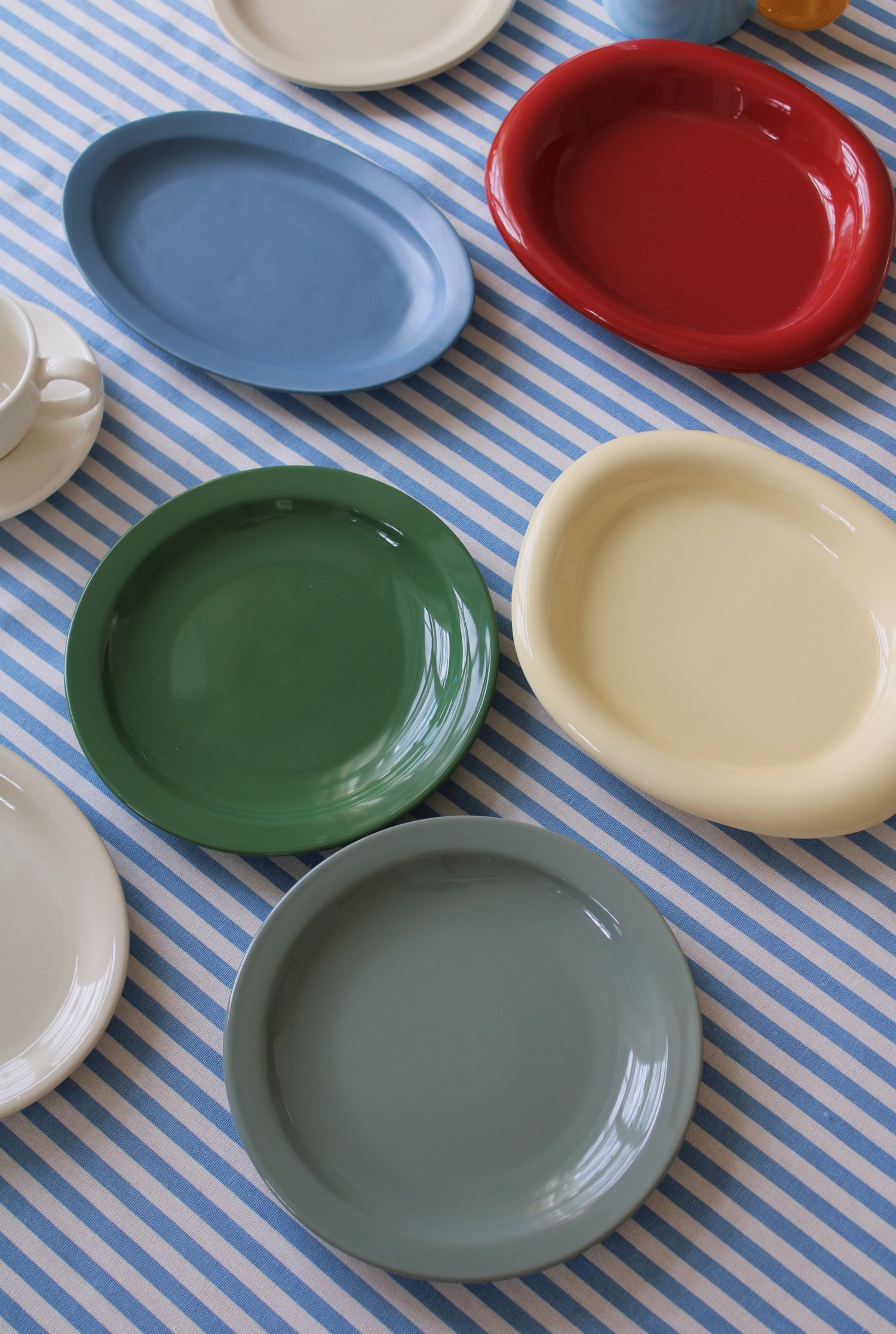 Colorful ceramic plates in soft blue, red, green, cream, and grey tones arranged on a blue striped tablecloth.
