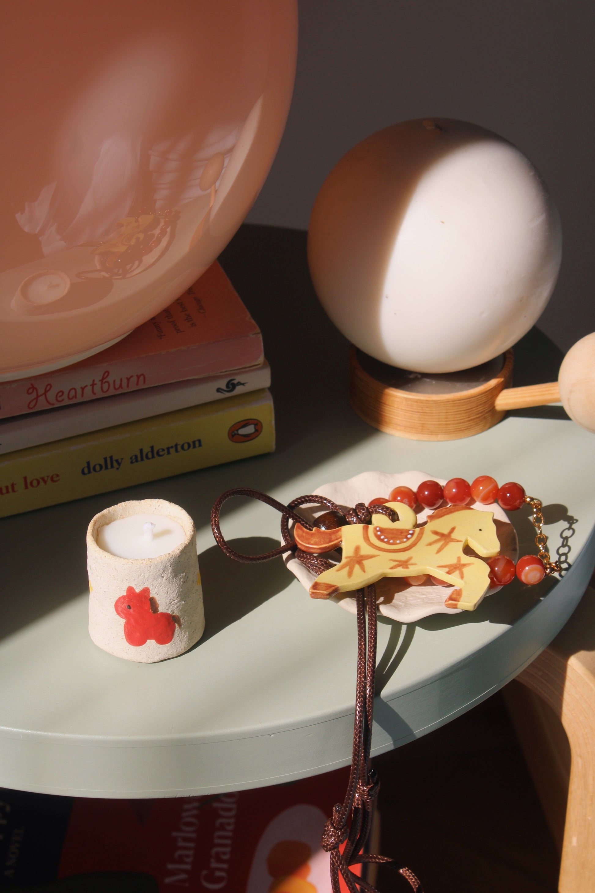 Small decorative item with a horse design on a surface with books and a lamp in the background.