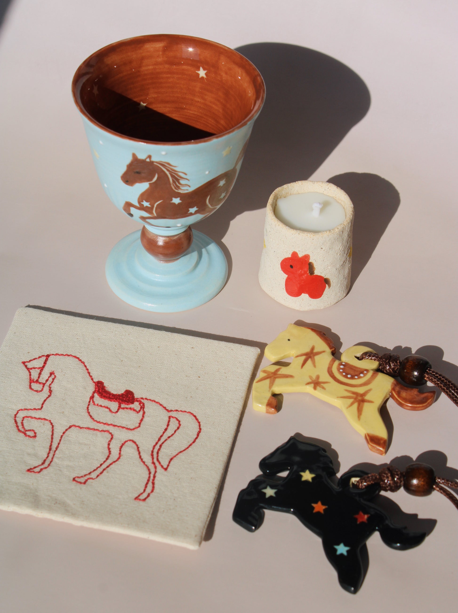Collection of horse-themed items including a ceramic cup, candle, keychain, and embroidered fabric on a light surface.