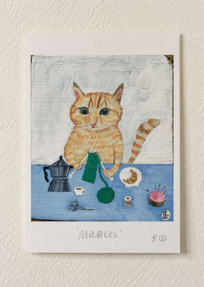 Marcel Cat Art Print featuring an orange tabby cat knitting green yarn at a blue table, surrounded by a moka pot, coffee cup, sewing supplies, scissors, and a small plate of pastries.