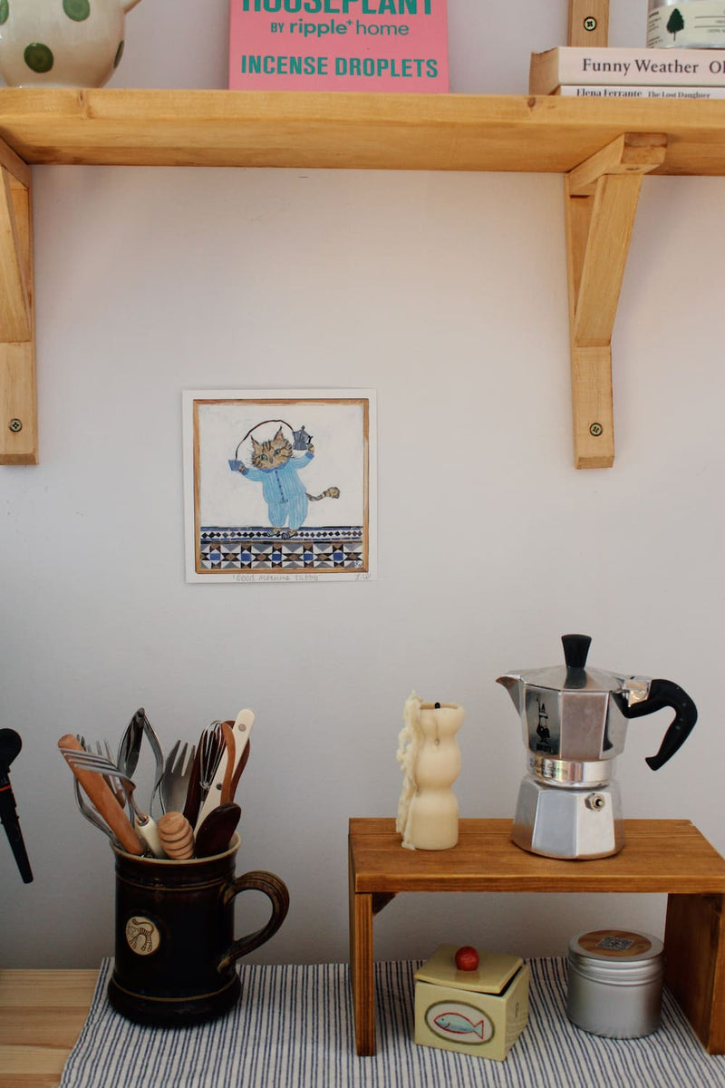 Good Morning Tabby Art Print – illustrated cat art print featuring two cats snuggled together in a blue blanket, styled above a colourful coffee station with ceramic mugs and home accessories