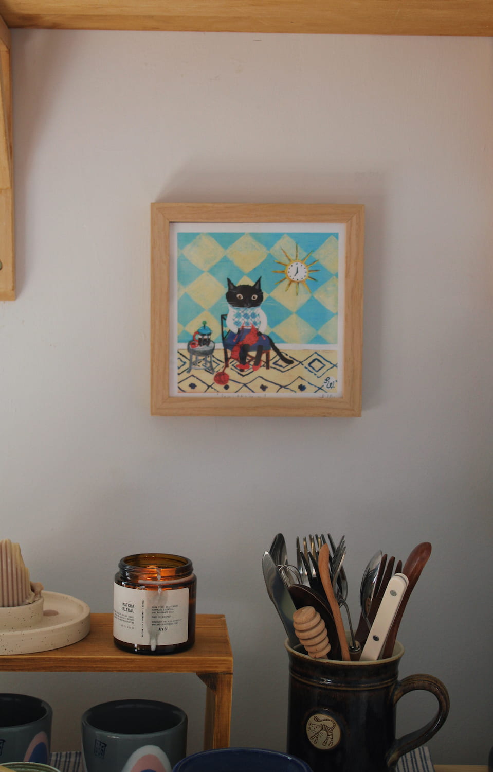 Knitting Cat Art Print – illustrated cat art print styled on a wall above a colourful coffee station with ceramic mugs, books and home decor