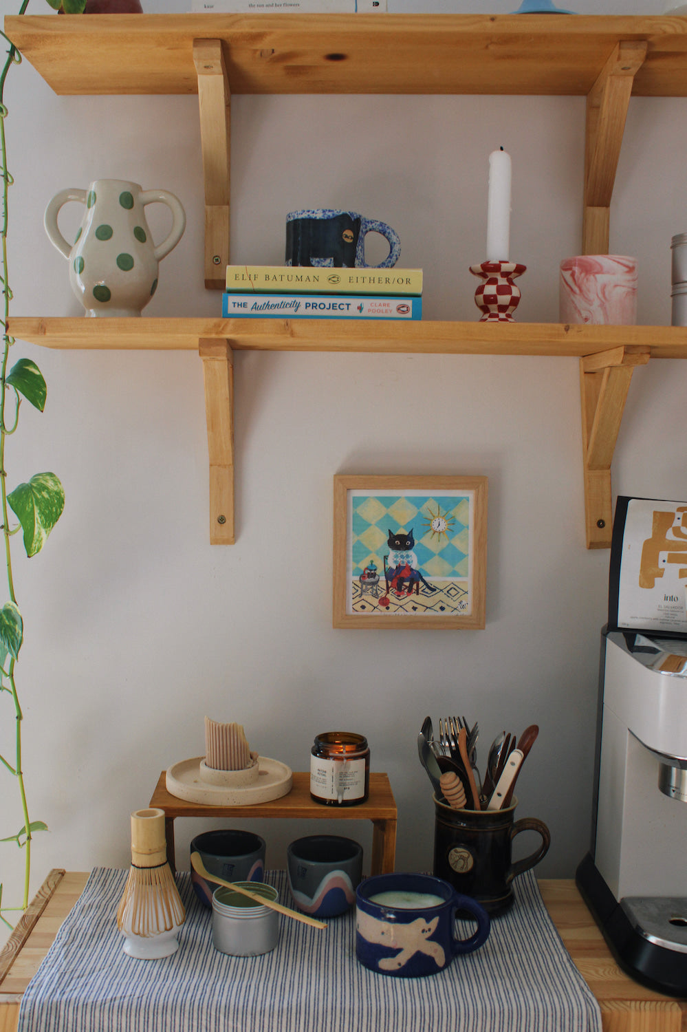 Knitting Cat Art Print – illustrated cat art print styled on a wall above a colourful coffee station with ceramic mugs, books and home decor
