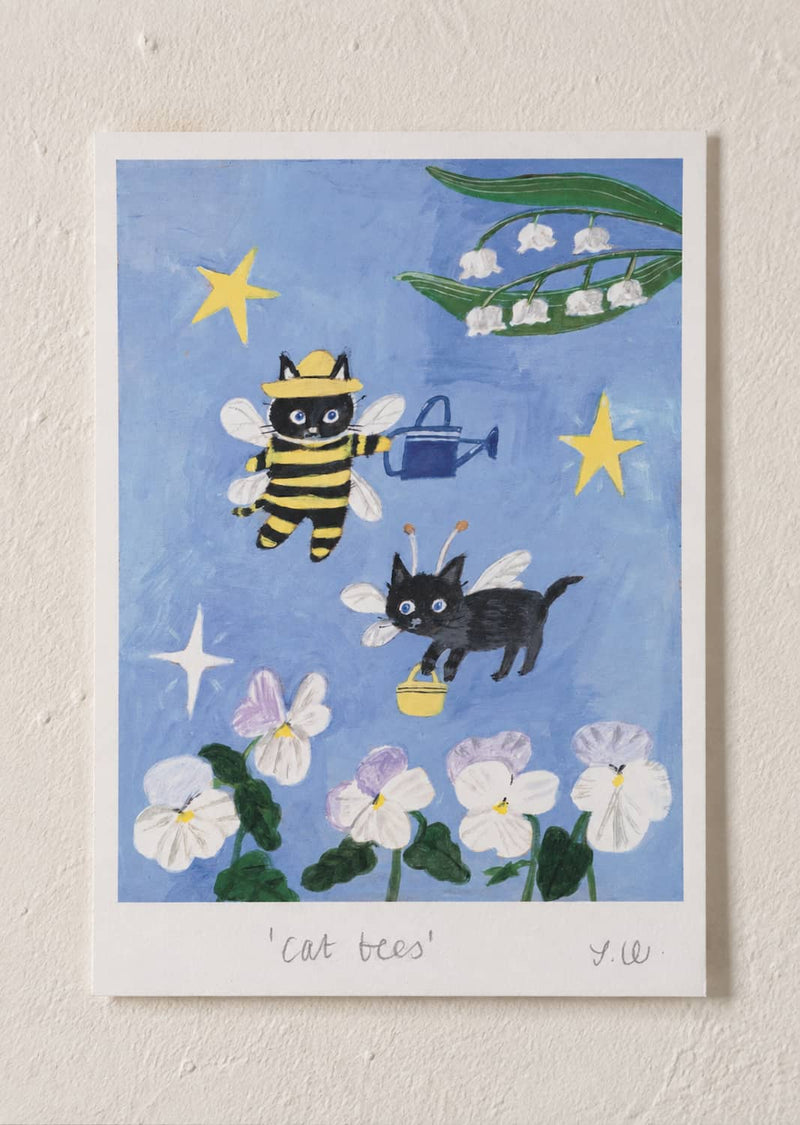 cat Bees Art Print featuring two playful black cats dressed as bees flying among flowers, stars, and lily of the valley blossoms against a blue background.