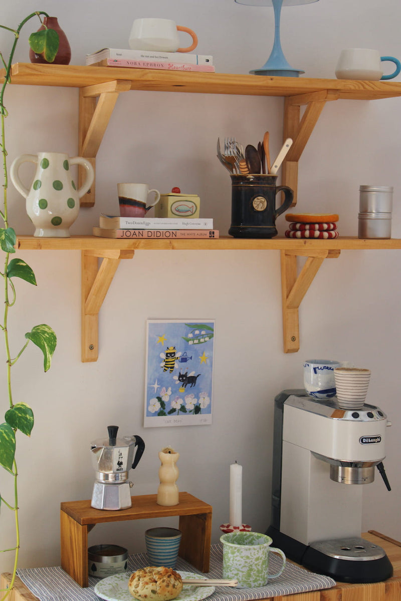 Cat Bees Art Print – illustrated art print featuring two black cats dressed as bees among flowers, styled above a coffee station with colourful ceramics and breakfast tableware