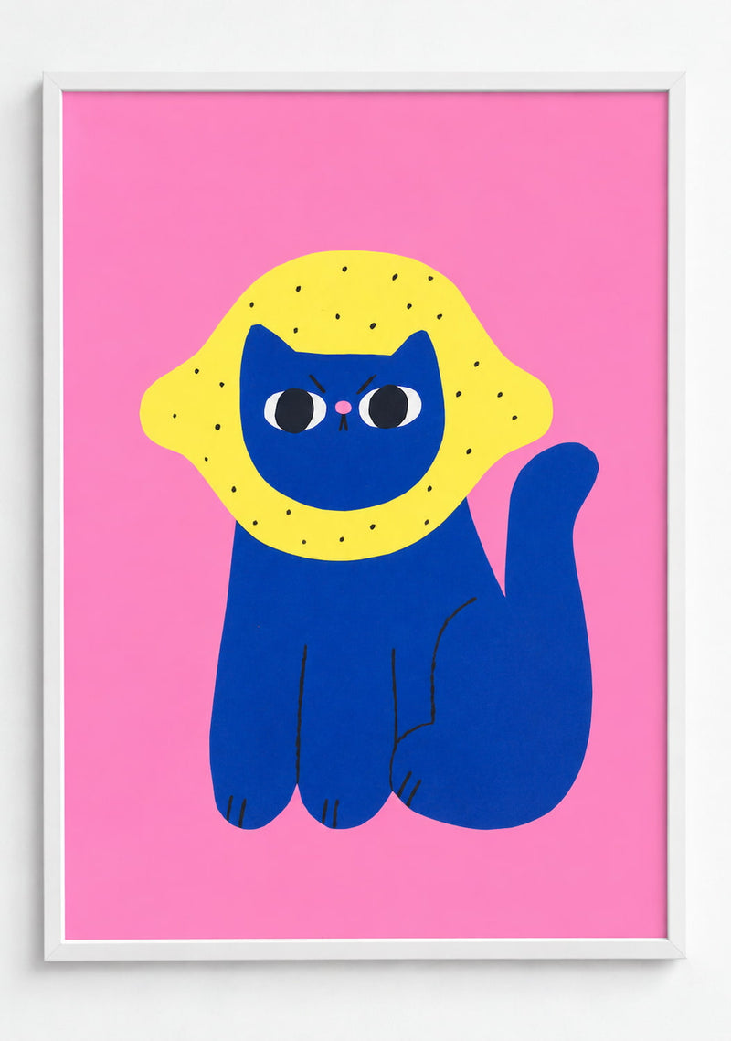 Lemon Cat Art Print- A framed minimalist art print featuring a blue cat wearing a yellow spotted hood or mask, set against a solid pink background. The print is enclosed in a thin white frame and shown against a clean white wall.