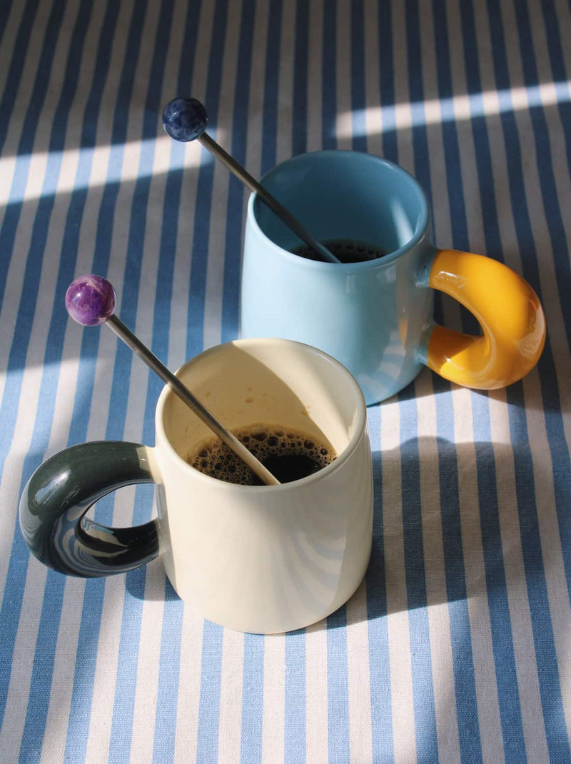 Astra drink stirrer set with ceramic cups and espresso on striped table setting.