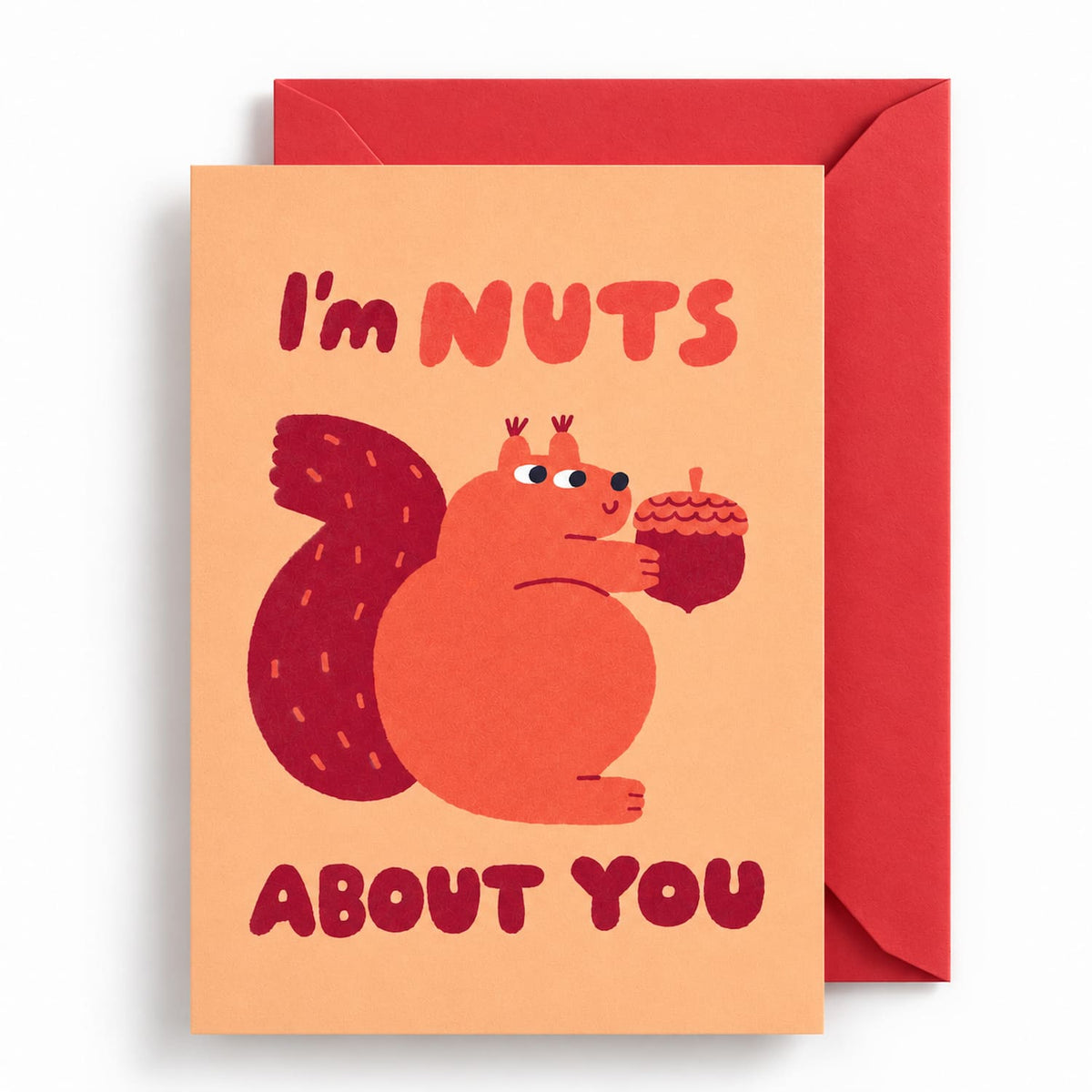 I’m Nuts About You greeting card featuring a playful orange squirrel holding an acorn, with bold retro lettering on a peach background and a red envelope.