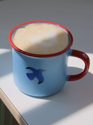 Birdie ceramic mug in warm sunlight, blue and red handmade mug for relaxed morning coffee