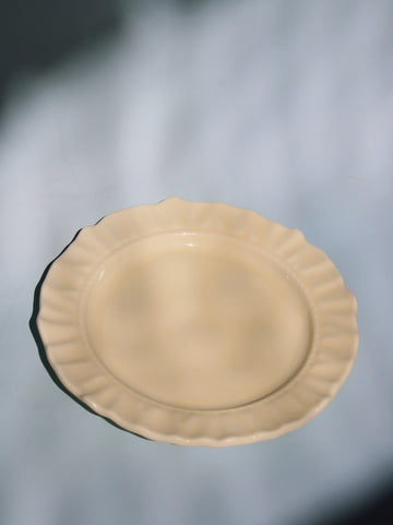 Beige ceramic plate with scalloped edge on a light gray background