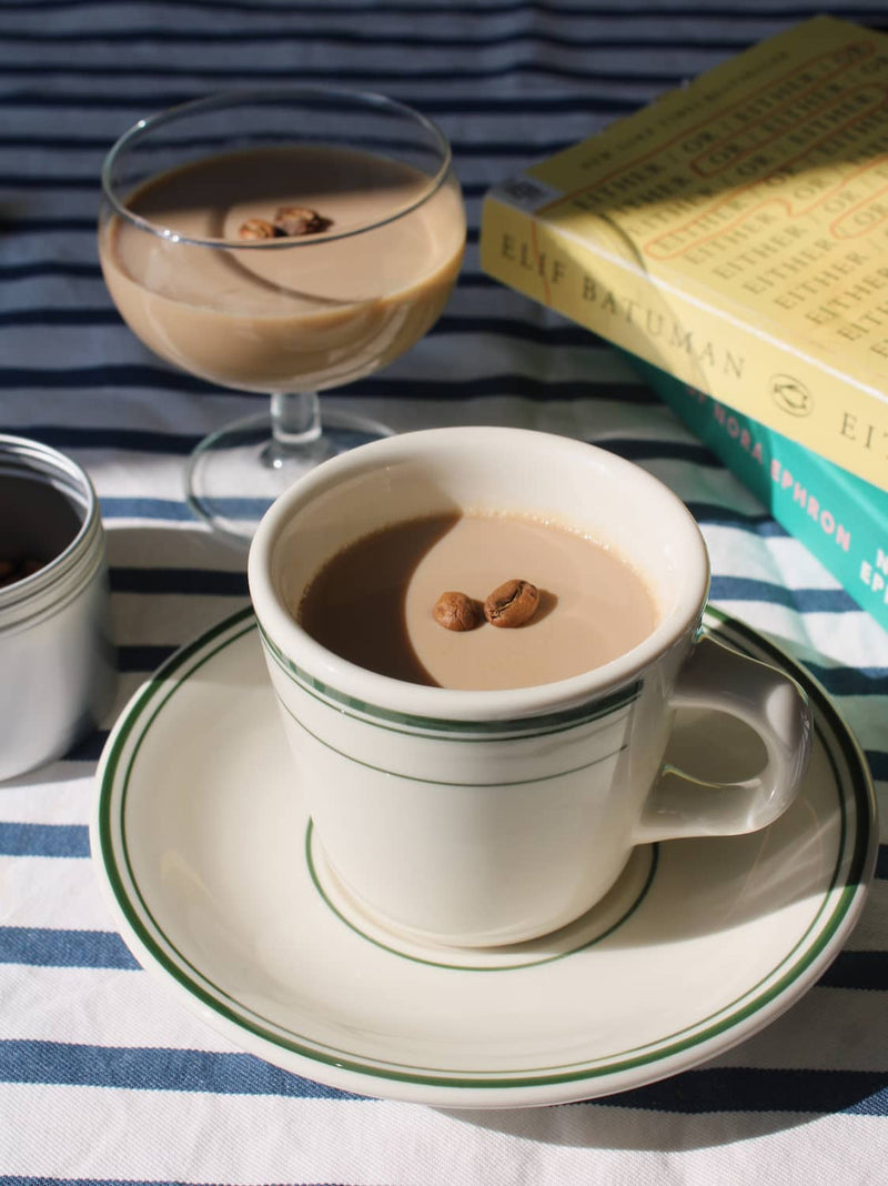 Verde cup and saucer set in cream ceramic with green stripe detail, styled with coffee and a wooden spoon