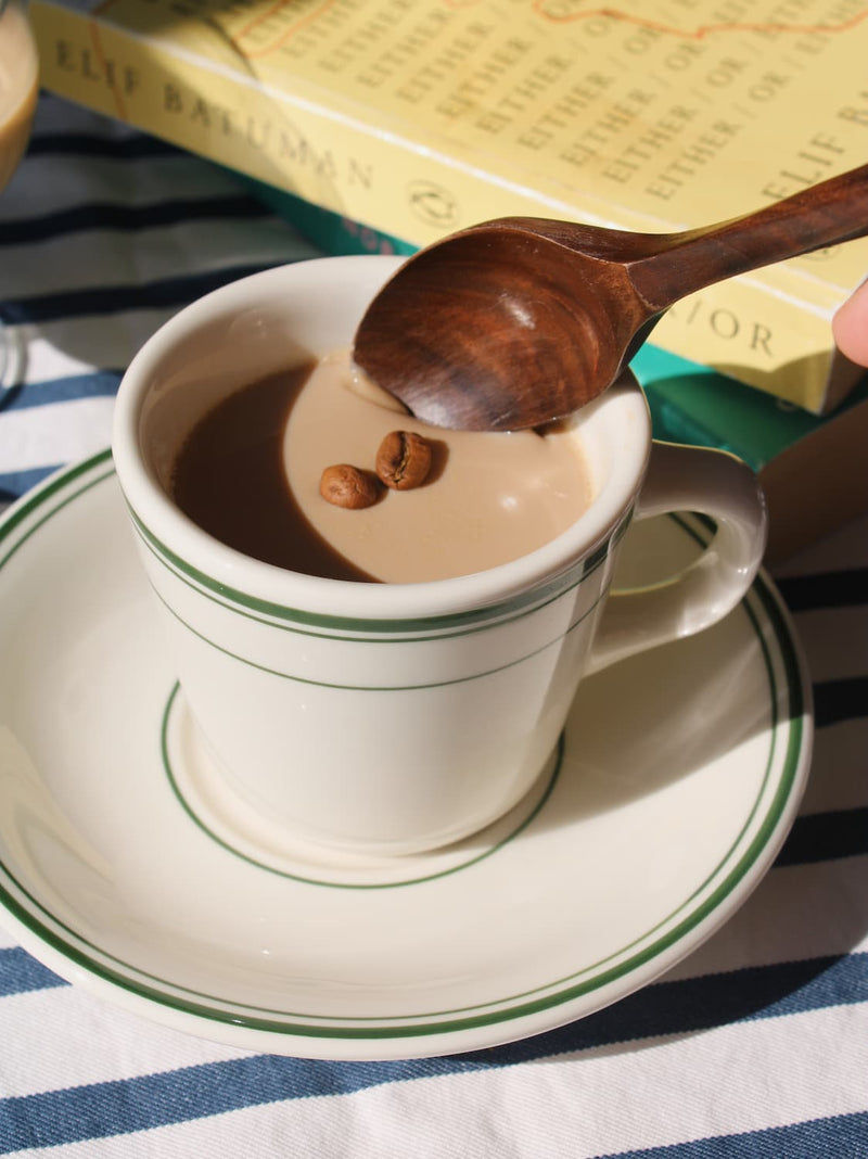 Verde cup and saucer set in cream ceramic with green stripe detail, styled with coffee and a wooden spoon