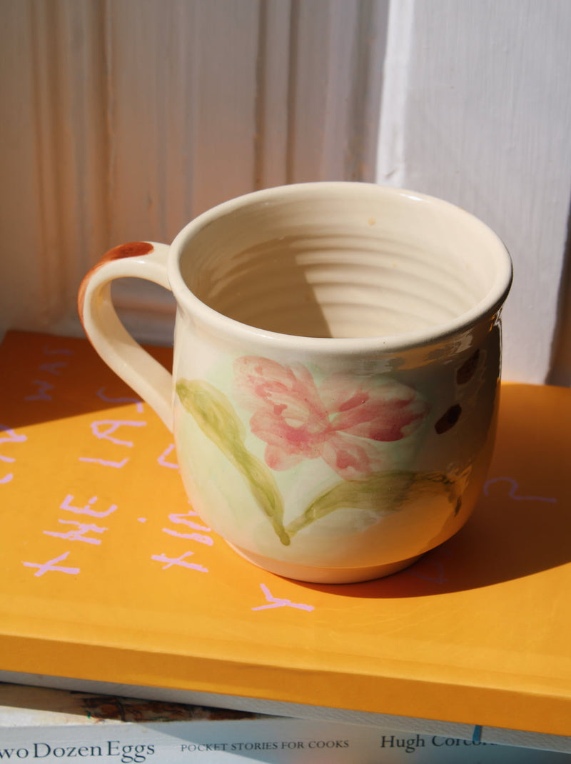 Handmade Camellia mug with soft pink flower motif styled on books.