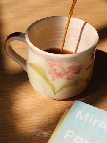 Camellia ceramic mug with coffee being poured in cozy morning light.