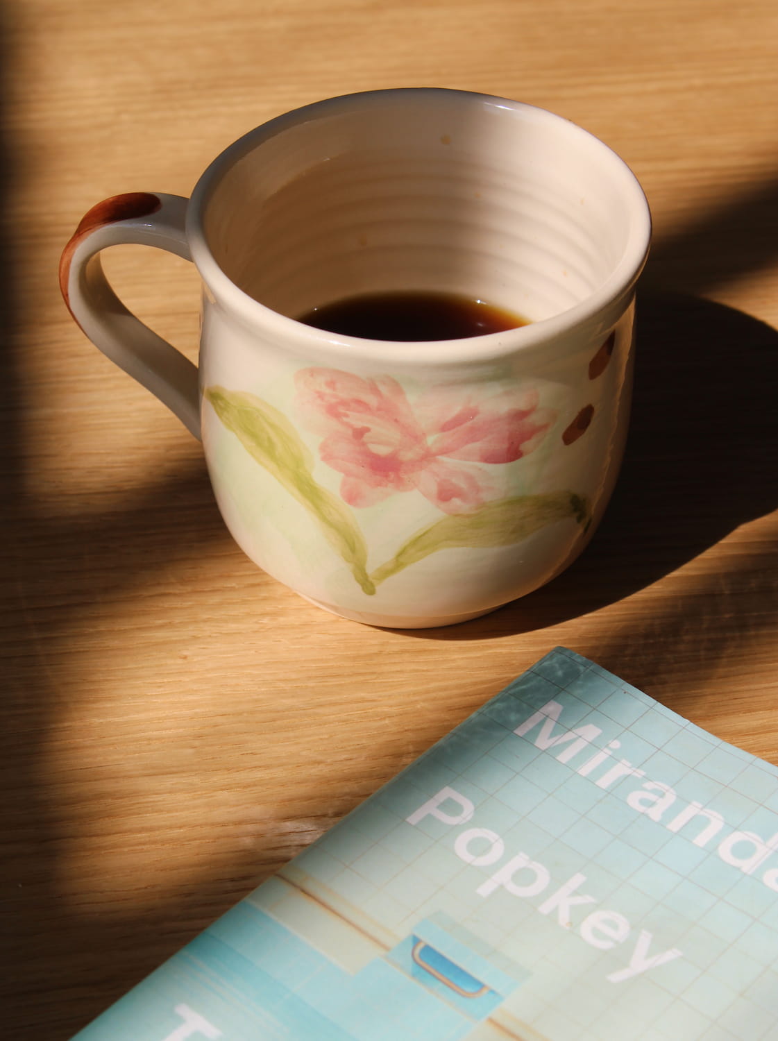 Camellia ceramic mug with hand-painted floral design on wooden table in warm sunlight.