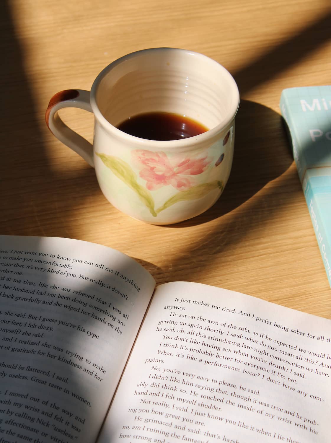Camellia ceramic mug with hand-painted floral design on wooden table in warm sunlight.