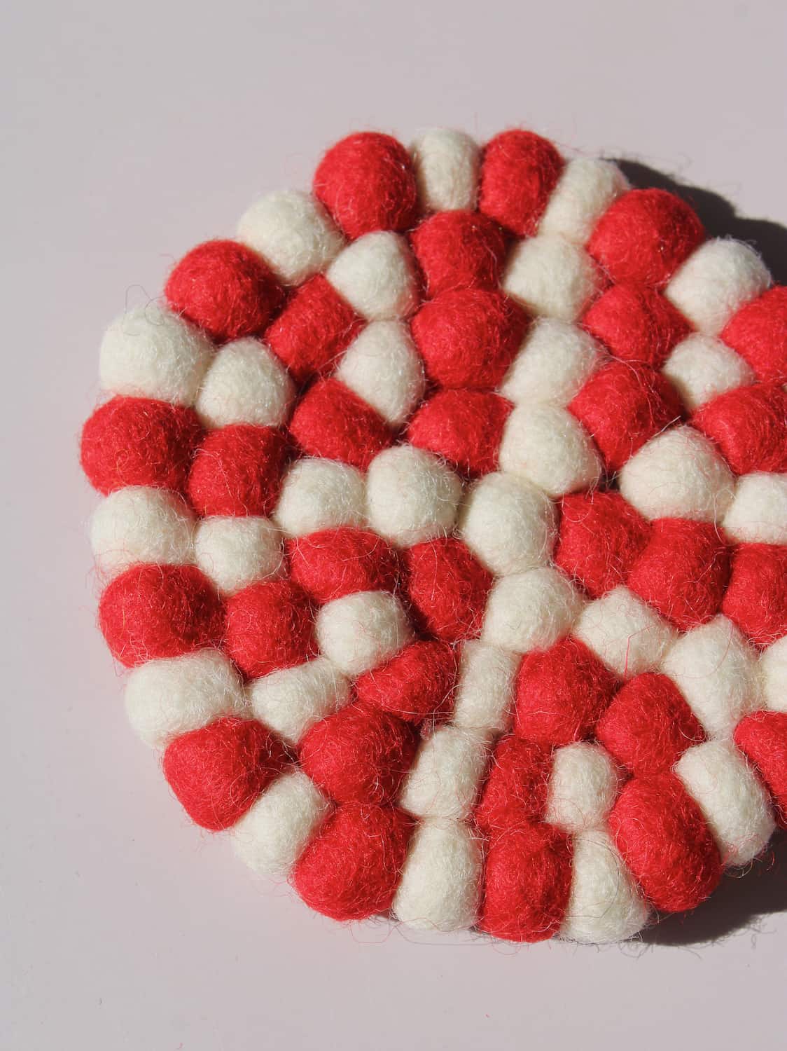 Bonbon Handmade Coaster made of red and white felted wool balls, candy-stripe pattern, top view