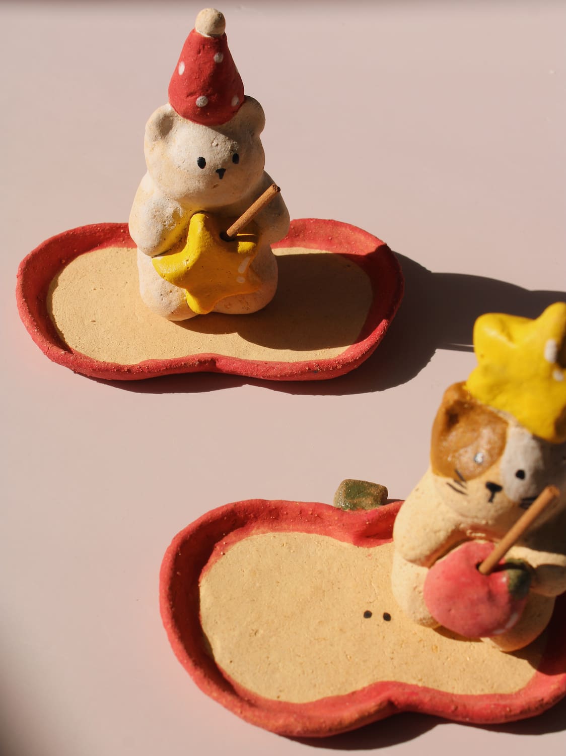 Teddy Ceramic Incense Holder and Mochi Ceramic Incense Holder, two handmade animal figurines with star and apple accents on matching apple-shaped incense trays, on a soft pink background.