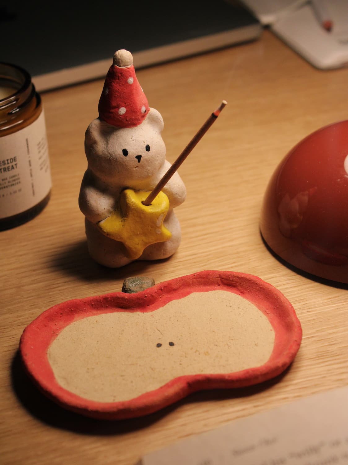 Teddy Ceramic Incense Holder with a lit incense stick, styled on a wooden surface with a candle and terracotta bowl in warm evening light.