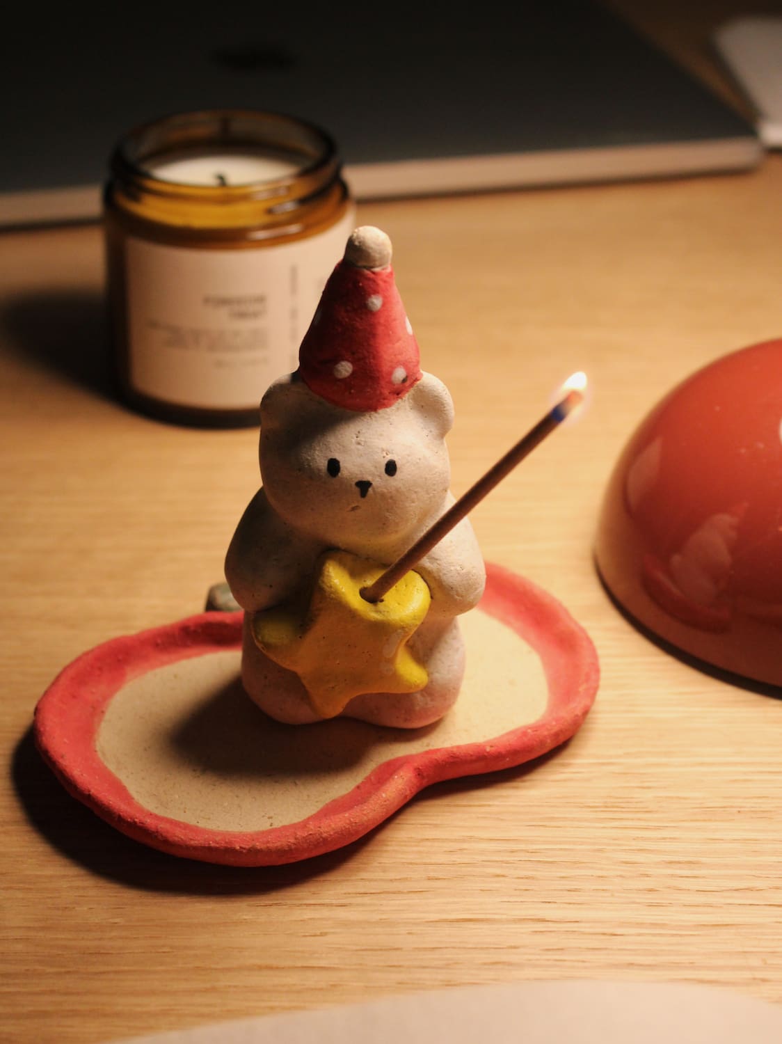 Teddy Ceramic Incense Holder with a lit incense stick, styled on a wooden surface with a candle and terracotta bowl in warm evening light.