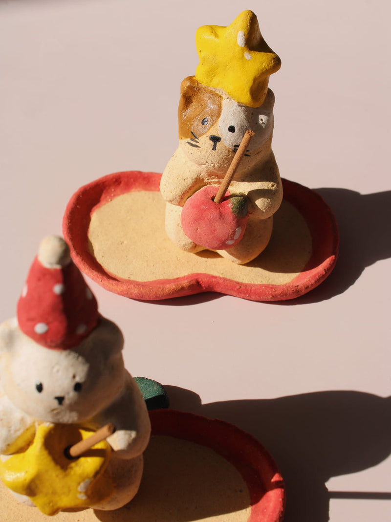 Mochi Ceramic Incense Holder, a handmade cat figurine wearing a yellow star hat and holding a pink apple, paired with an apple-shaped incense tray, on a soft pink background.