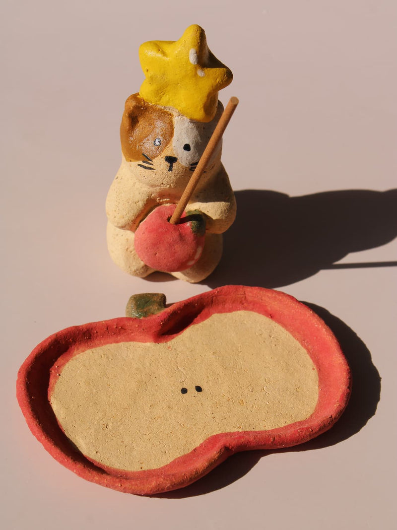 Mochi Ceramic Incense Holder, a handmade cat figurine wearing a yellow star hat and holding a pink apple, paired with an apple-shaped incense tray, on a soft pink background.