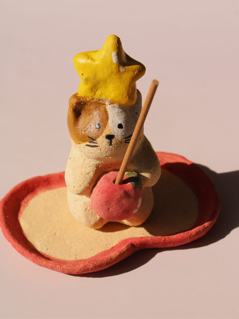 Mochi Ceramic Incense Holder, a handmade cat figurine wearing a yellow star hat and holding a pink apple, paired with an apple-shaped incense tray, on a soft pink background.