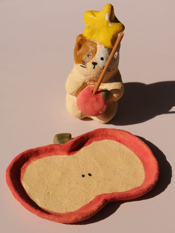Mochi Ceramic Incense Holder, a handmade cat figurine wearing a yellow star hat and holding a pink apple, paired with an apple-shaped incense tray, on a soft pink background.