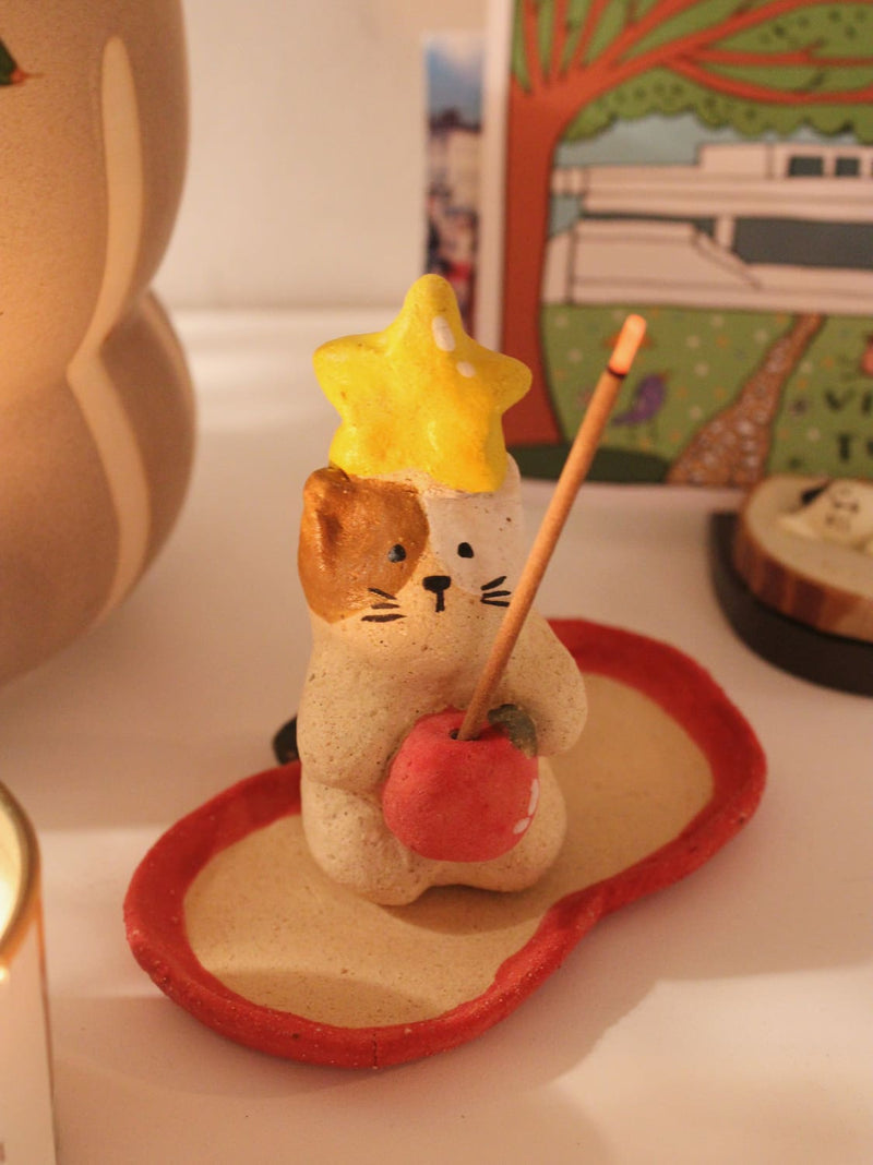 Mochi Ceramic Incense Holder with a lit incense stick, styled on a shelf with colourful artwork and a terracotta vase in the background in warm indoor light.