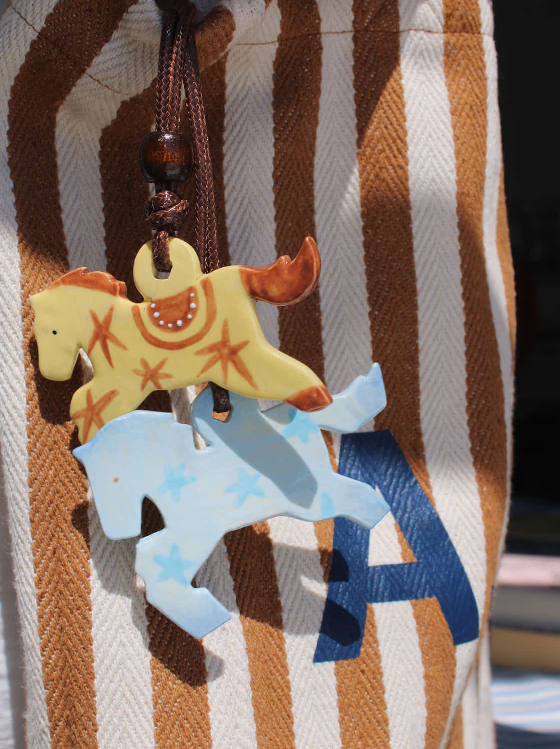 Stardust Pony Charm and Amber Pony Charm layered together as a bag charm on a striped canvas tote in natural sunlight.