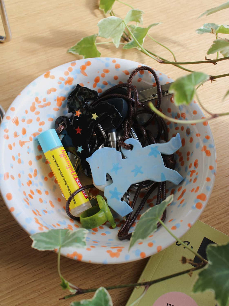 Stardust Pony Charm Necklace and Midnight Pony Charm Necklace resting in the Naro Ceramic Bowl alongside everyday items on a wooden surface with trailing ivy.