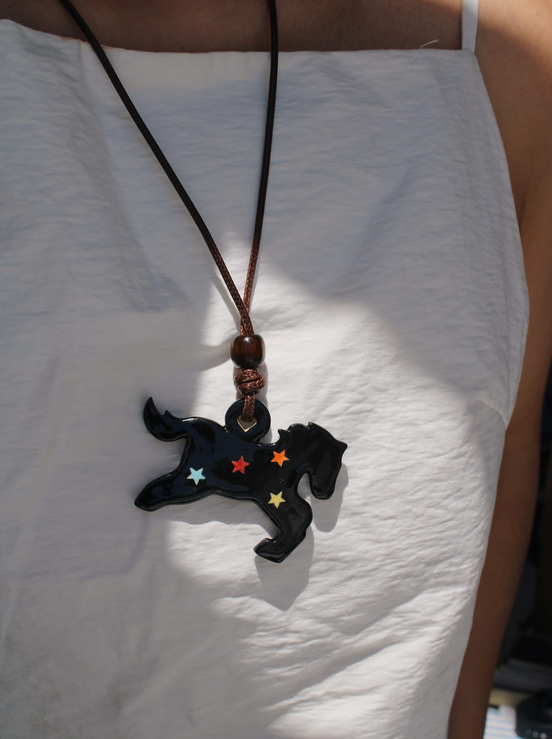 Midnight ceramic charm necklace in glossy black with star details, worn on a leather cord against a white top