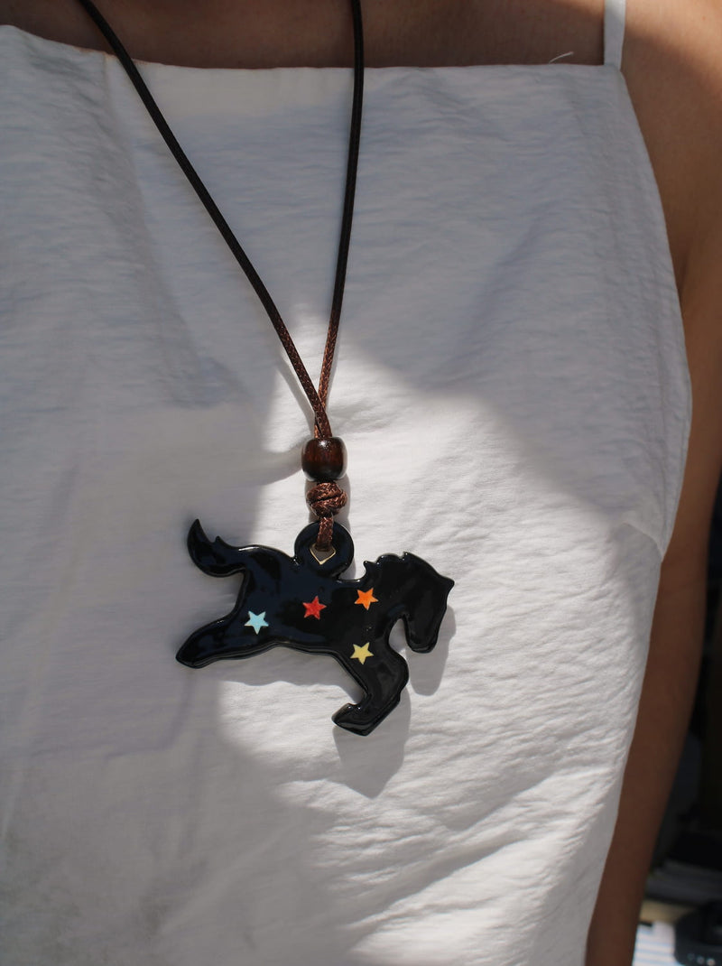 Midnight ceramic charm necklace in glossy black with star details, worn on a leather cord against a white top