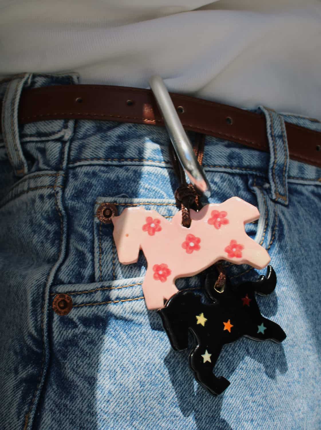 Petal Pony and Midnight ceramic charm necklaces side by side, pink floral and black star motifs on leather cords, styled against denim jeans