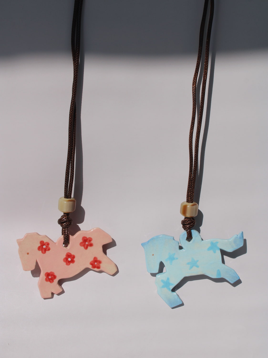 Petal Pony and Stardust Pony Charm Necklaces side by side, pink floral and blue starry ceramic horse pendants
