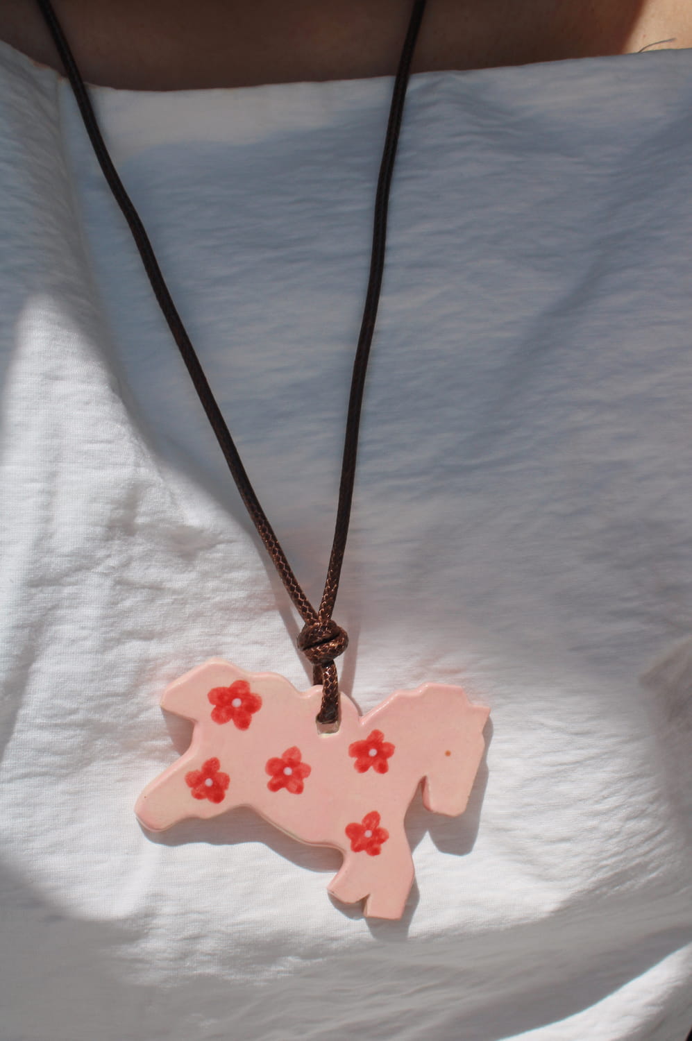 Petal Pony ceramic charm necklace in soft pink with floral motifs, worn on a leather cord against a white top
