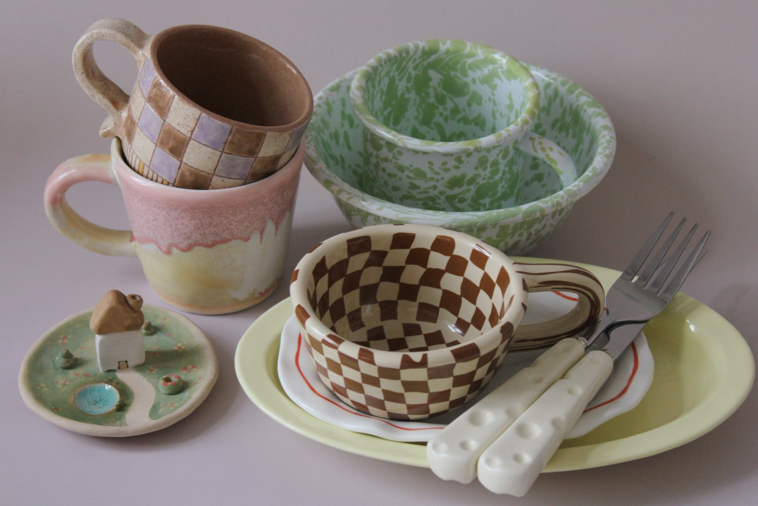 Set of ceramic tableware including cups, bowls, and a fork on a neutral background