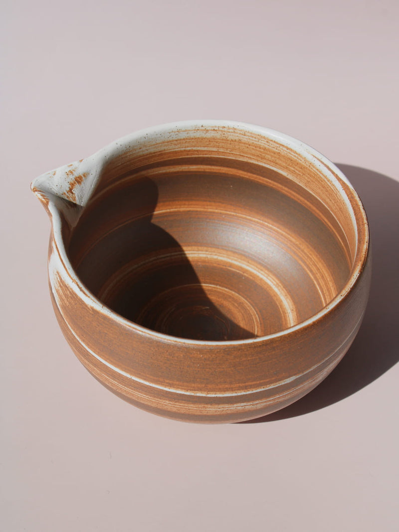 Kanso Matcha Bowl in warm terracotta with white swirl glaze detail and a pouring spout, on a soft pink background.