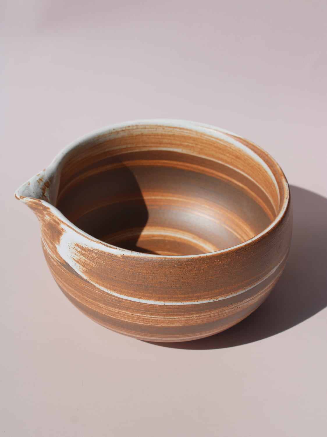Kanso Matcha Bowl in warm terracotta with white swirl glaze detail and a pouring spout, on a soft pink background.