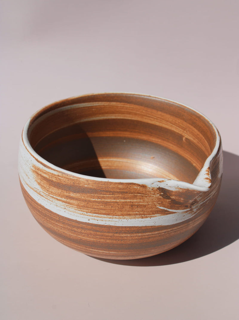 Kanso Matcha Bowl in warm terracotta with white swirl glaze detail and a pouring spout, on a soft pink background.